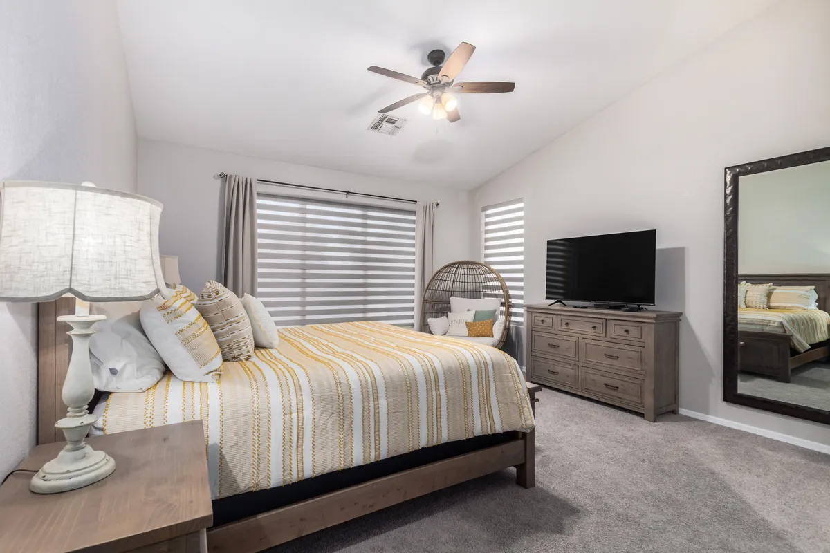 This image shows a bedroom with yellow and white striped bedding, a whimsical hanging chair (egg chair), a large mirror, and a TV on a dresser. The space feels comfortable, inviting, and serene, with soft lighting and modern furnishings.
