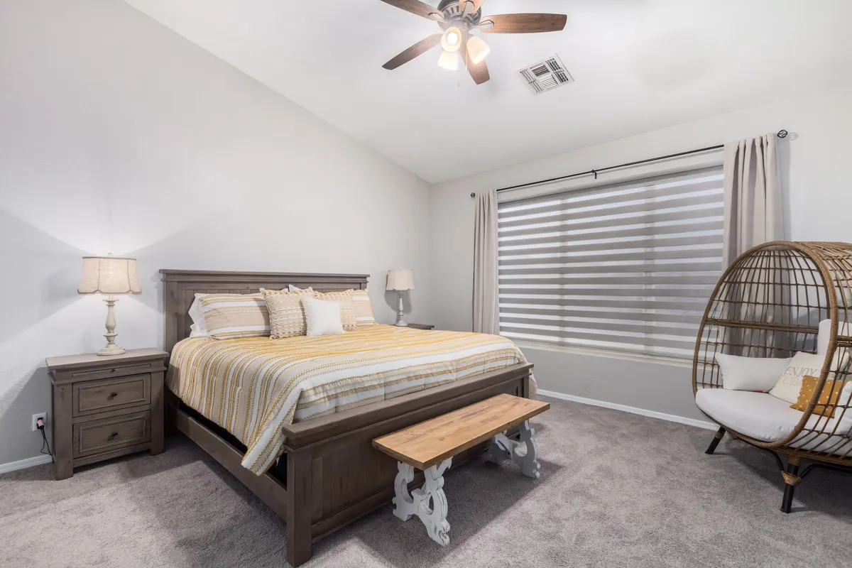 A queen bedroom featuring striped bedding, a unique hanging chair, a wooden bench, and a nightstand with a lamp. The room feels calm, restful, and welcoming, with accents that make it appealing for both kids and adults.