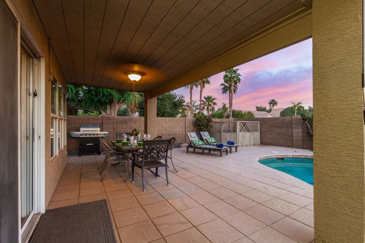 An outdoor dining area set beside a sparkling swimming pool, complemented by lounge chairs, a grill, and beautiful landscaping. The space is designed for both relaxation and entertaining, evoking the idea of taking breaks or celebrating the end of a productive workday.
