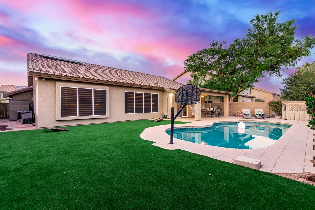 This exterior image features a sparkling swimming pool with a basketball hoop, an outdoor seating area, and a well-maintained landscaped lawn. The scene highlights recreational opportunities with space for both swimming and sports while offering areas for relaxation and social gatherings.