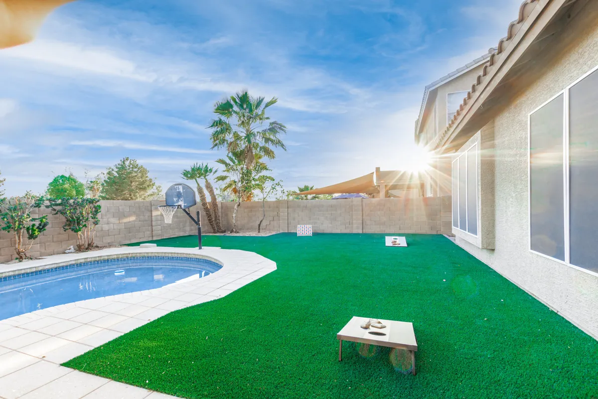 A playful backyard view featuring a swimming pool with a basketball hoop, artificial grass lawn, and a cozy outdoor seating area. The scene radiates both relaxation and opportunities for energetic play, framed by the warm Arizona light.