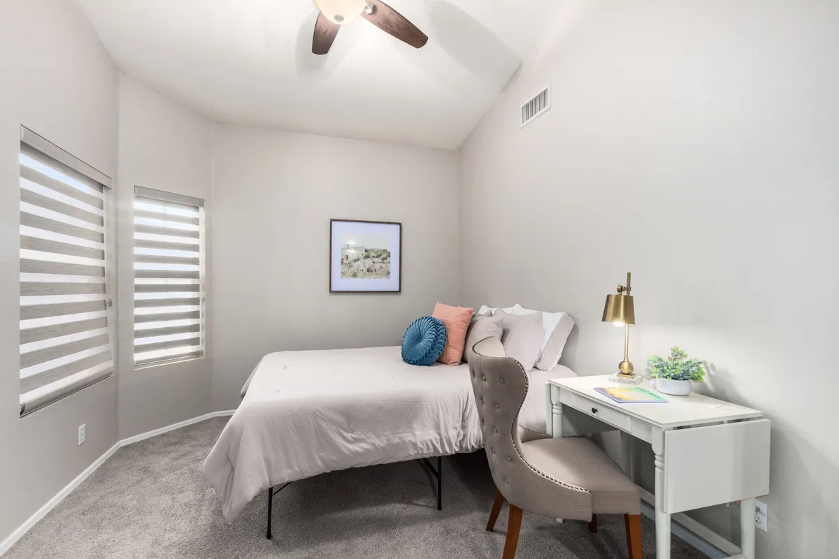 A tranquil bedroom with a queen bed, a small desk and chair, and decorative touches. Natural light filters in, creating a peaceful workspace or guest bedroom setting.