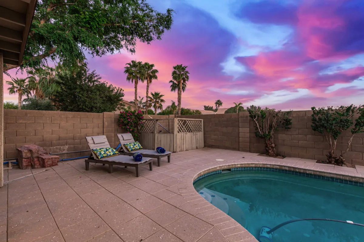 A serene backyard view with a glistening pool, palm trees swaying in the breeze, lounge chairs, and a vibrant, colorful sky at sunset. The tranquil atmosphere underscores the restorative benefits of outdoor living.