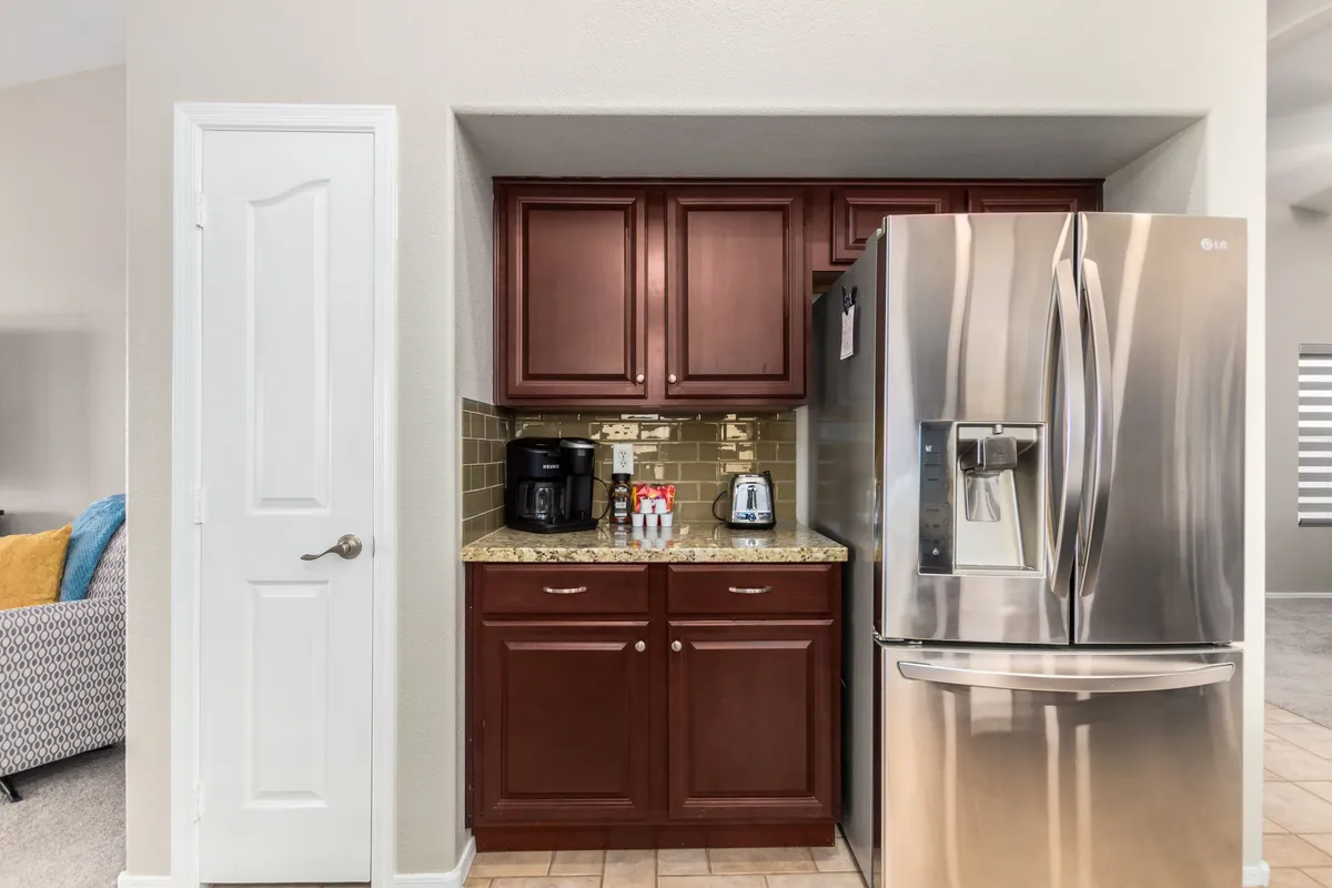 A cozy kitchen vignette focusing on the stainless steel refrigerator, a Keurig coffee maker on the granite countertop, and warm cabinetry. The setup is inviting for morning routines and quick coffee breaks.
